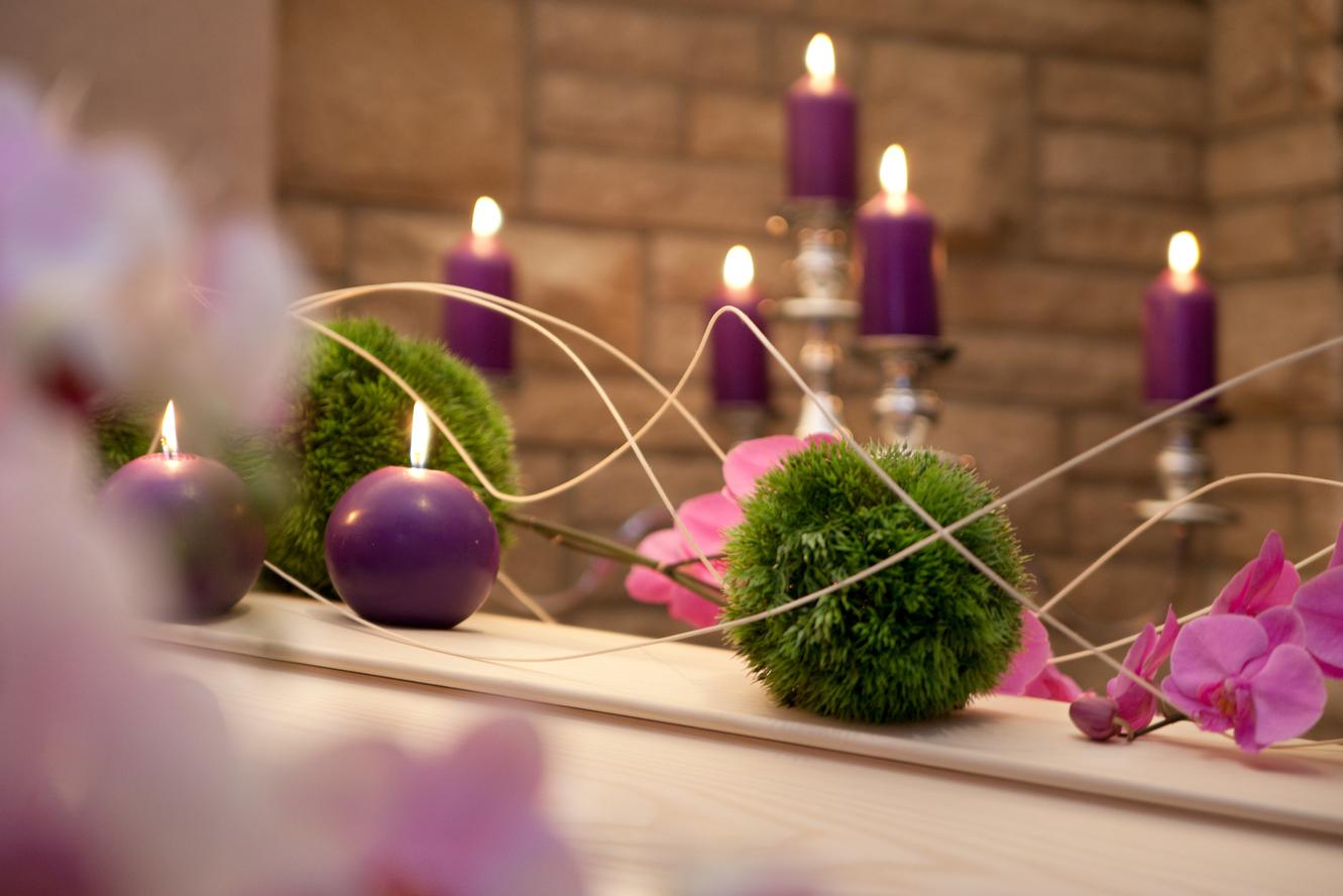 Dekorativer Tisch mit lila Kerzen, grünen Kugeln aus Moos und pinken Orchideenblüten in einem gemütlichen Ambiente.